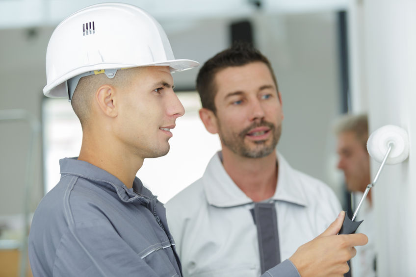 man supervising an apprentice painter using a roller